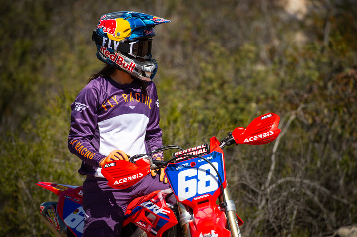 Woman on Honda CRF250R wearing Fly Racing gloves, jersey, helmet, and goggles. The red dirtbike has acerbis handguards and renthal handlebar guard